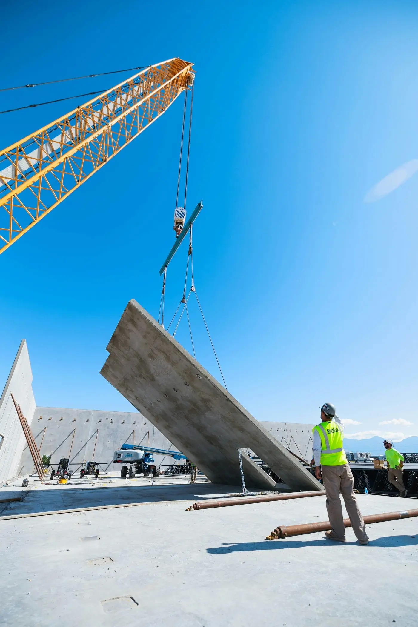 Une grue lève un panneau de béton sous le contrôle d'un compagnon